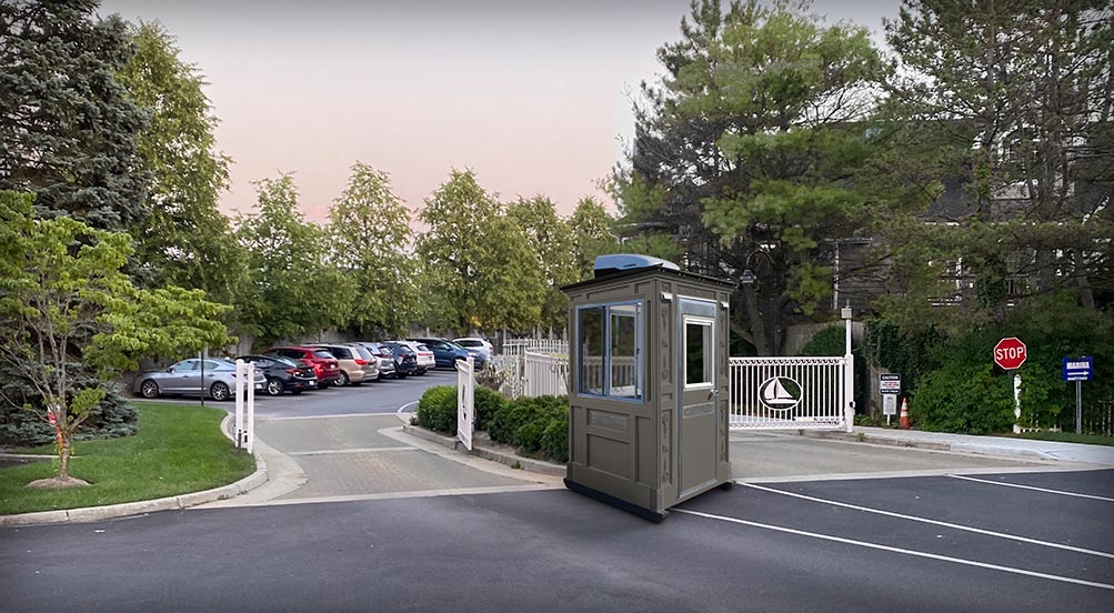 Security Guard Shed | The Guard Post 16 with a grey color, in front of a gated entrance with parking.