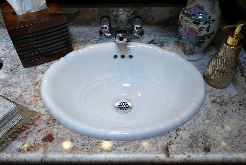 PORCELAIN VICTORIAN STYLE SINK ATOP A RICH MARBLE SLAB