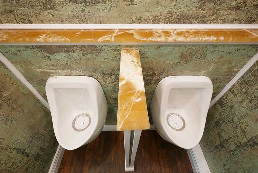 TWO PORCELAIN URINALS WITH A MARBLE CAPPED PRIVACY DIVIDER AND CONVENIENCE SHE